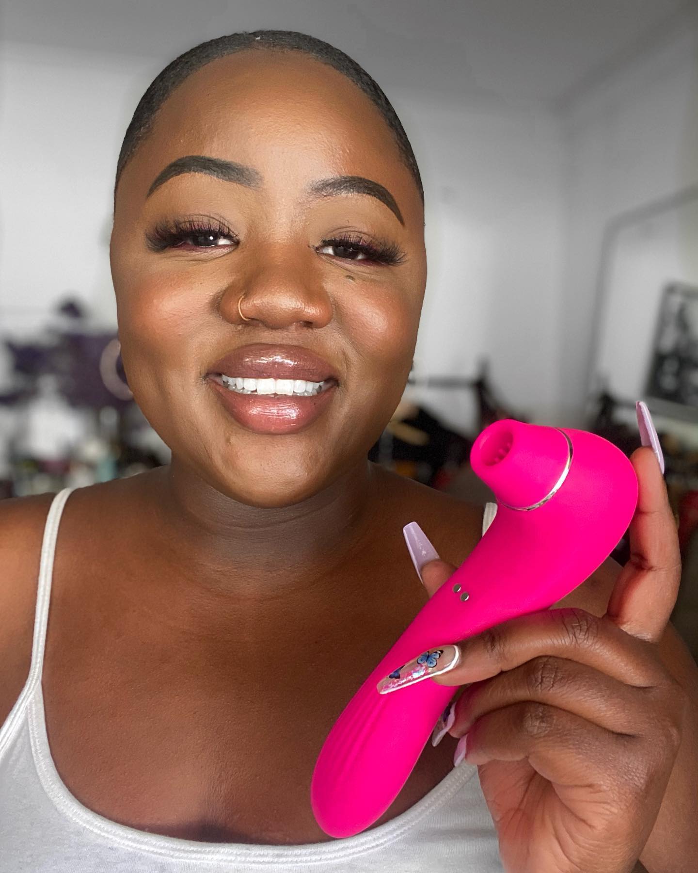 Bright pink facial cleansing device held by a smiling woman with long nails.