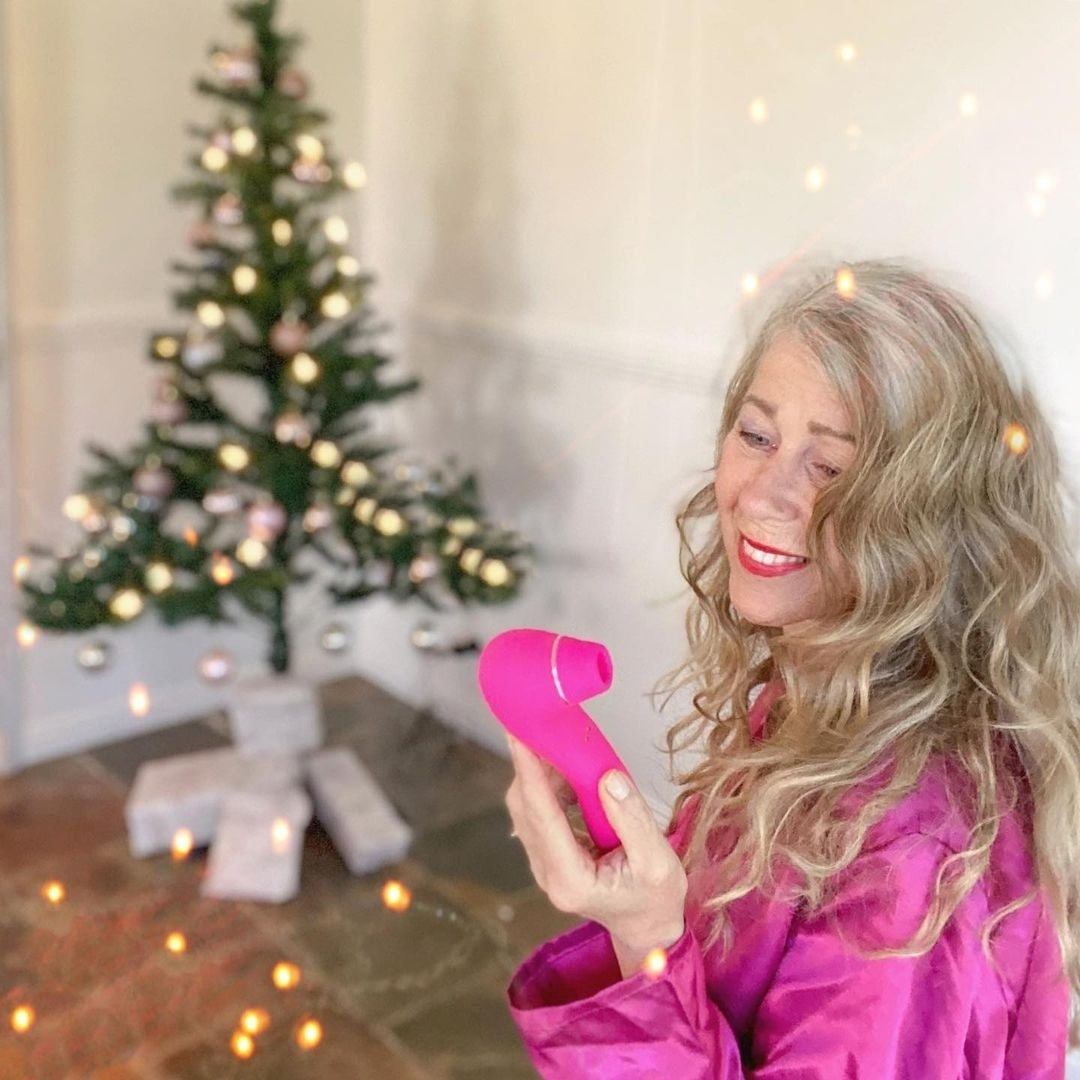 Pink facial cleansing brush held by a woman with long, wavy hair in a decorated holiday setting