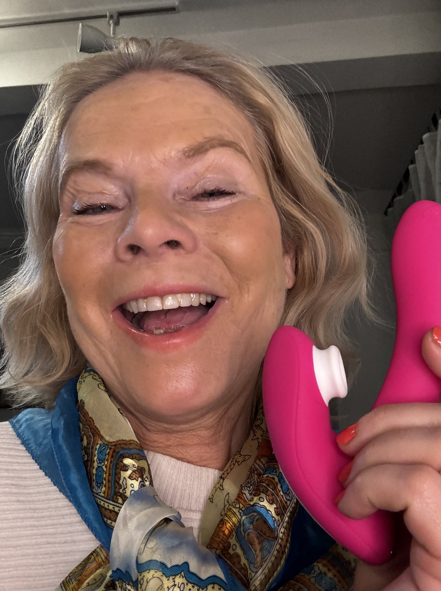 Smiling woman holding a pink massage device, wearing a patterned scarf.