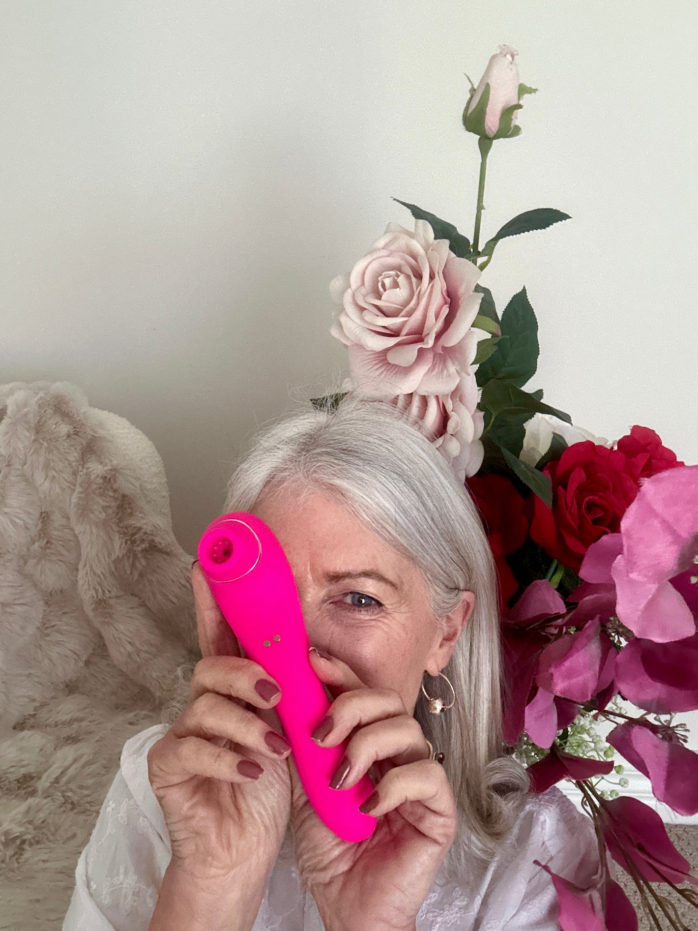 Bright pink personal massager held by a woman surrounded by pink and red flowers.