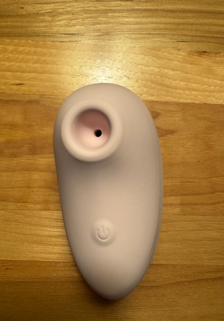 Pink silicone facial cleansing device with a power button and a curved ergonomic shape.
