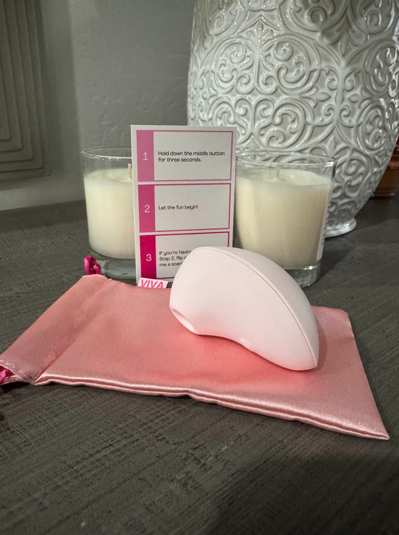Pink handheld skincare device with satin pouch and instruction card beside white candles.