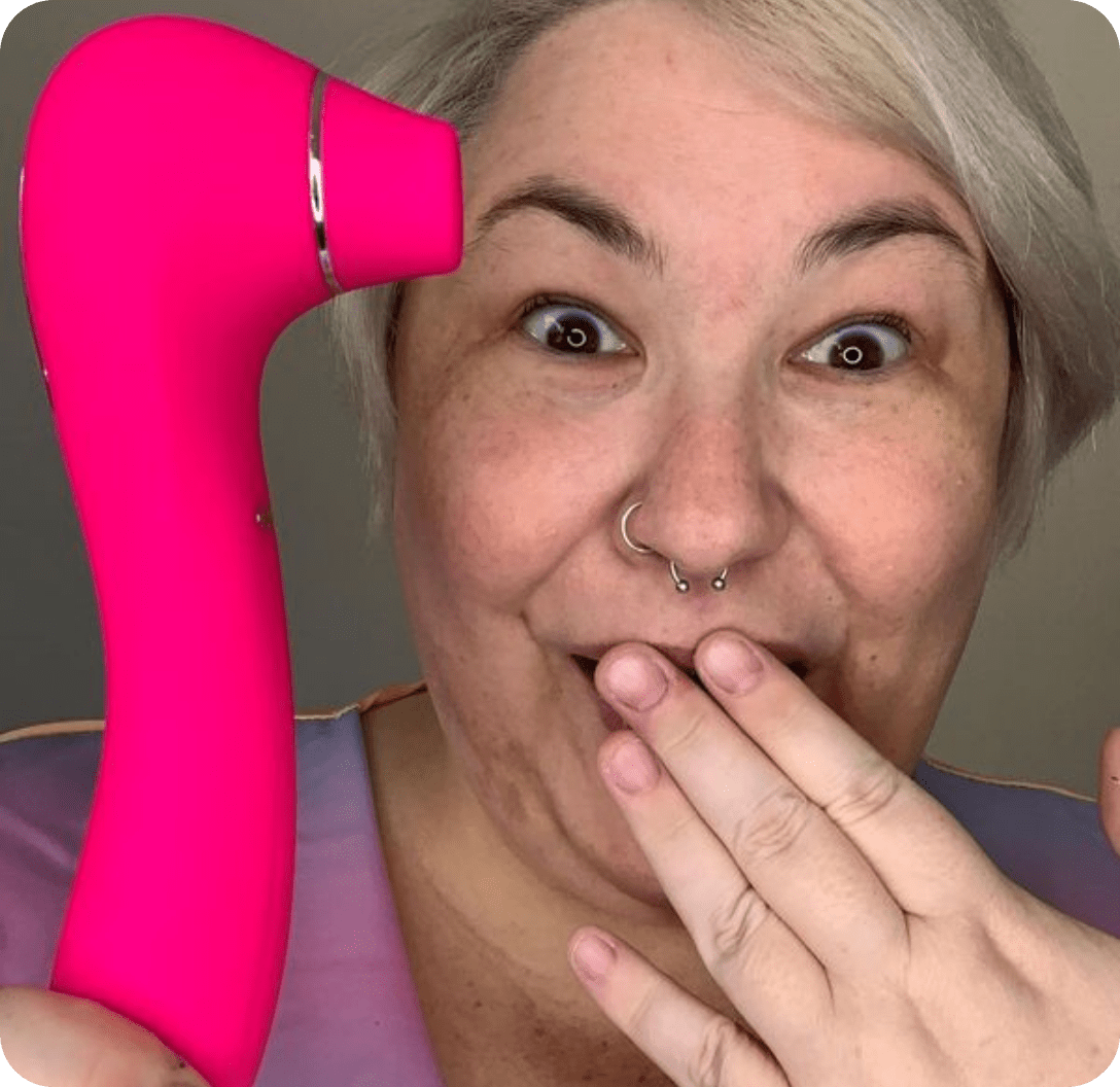 Bright pink facial cleansing device with curved design, held by a smiling person with short hair and piercings.